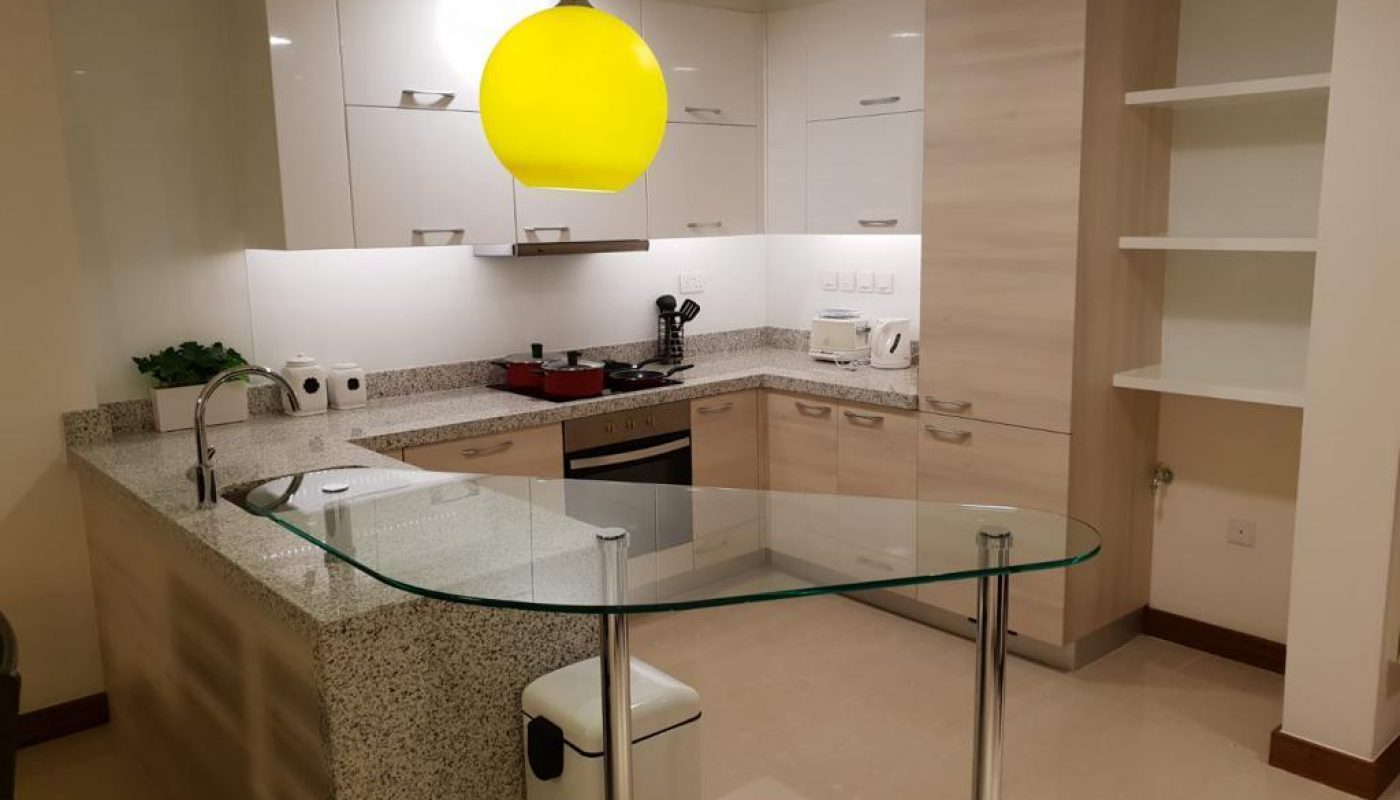 Modern kitchen with white cabinets, granite countertops, built-in appliances, a yellow pendant light, and a glass breakfast bar. Shelves are on the right wall.