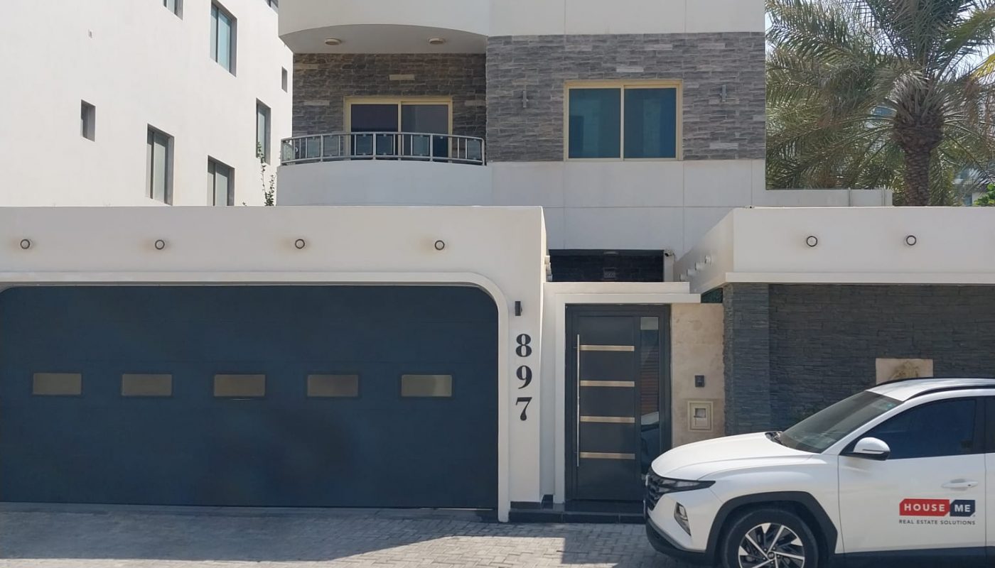 A modern three-story house with a gray and white facade, a large garage door, and a white SUV parked in front. The address number 897 is displayed by the entrance.
