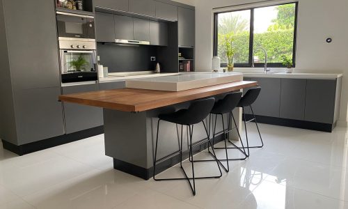 A fully furnished modern kitchen with a black island and stools in a villa.