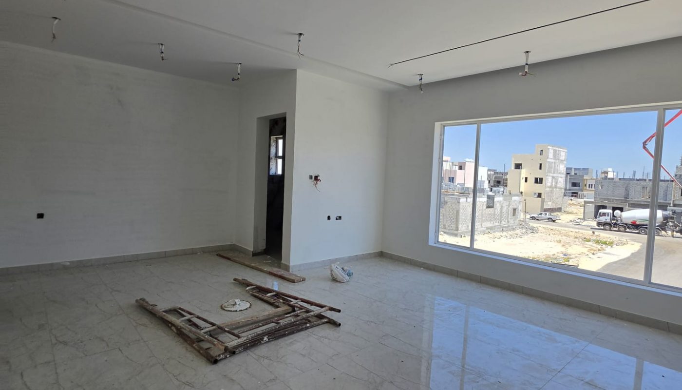 Unfurnished room with marble flooring, large window, and exposed ceiling wiring. Construction materials are placed on the floor near the center.