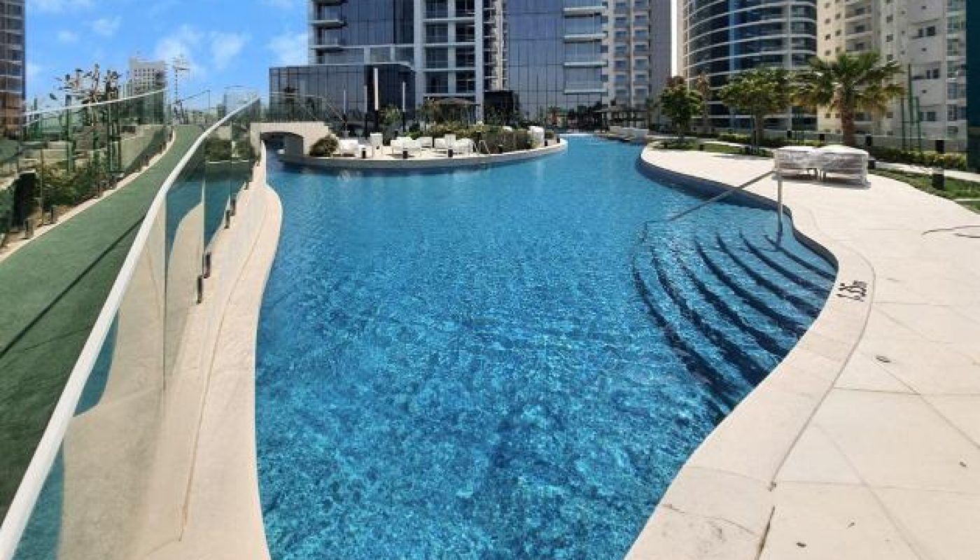 Rooftop infinity pool with clear blue water, surrounded by modern high-rise buildings under a partly cloudy sky.