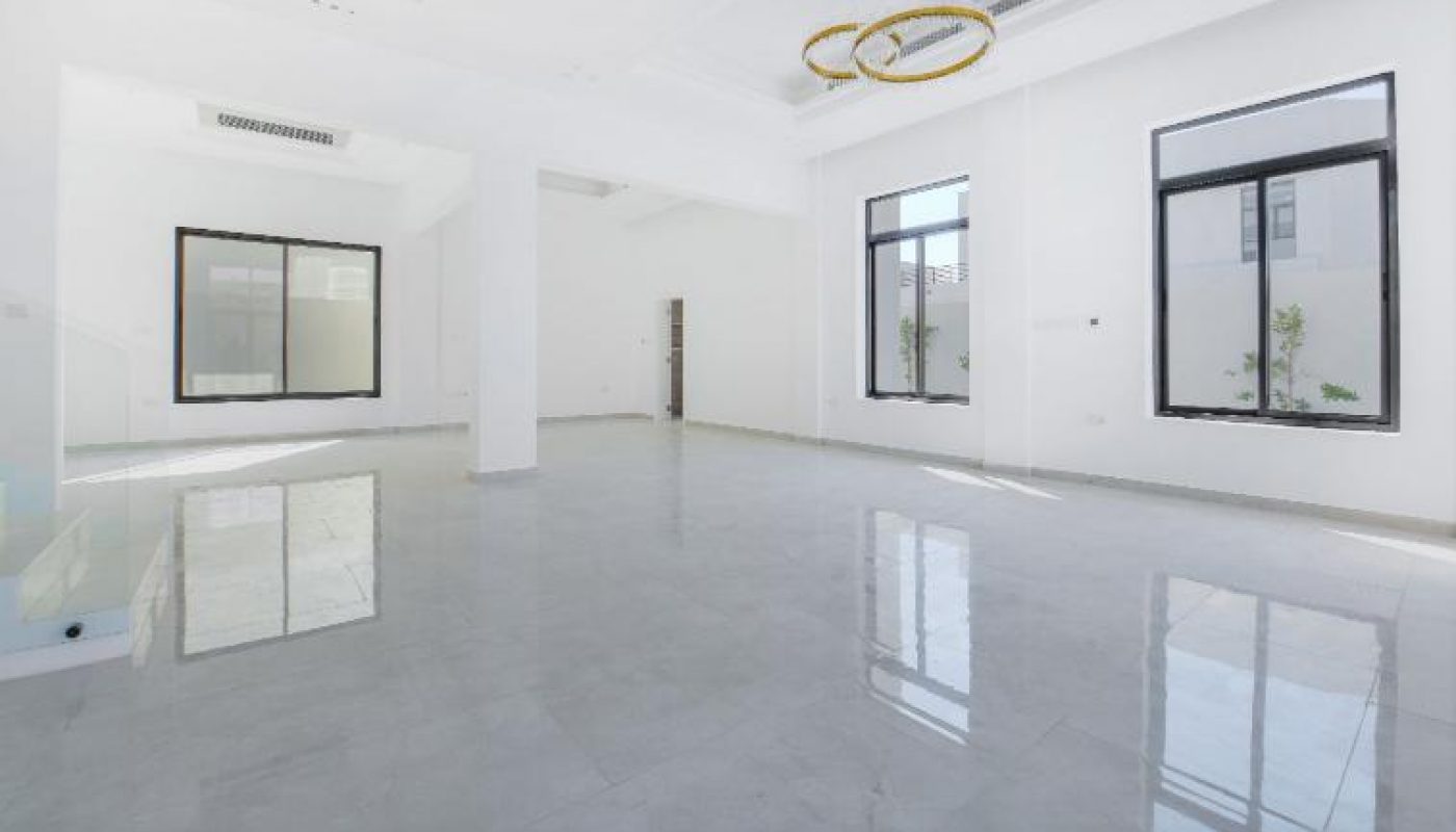 Spacious, empty modern living room with white walls, large windows, glossy tiled floor, recessed ceiling, and a gold circular chandelier.