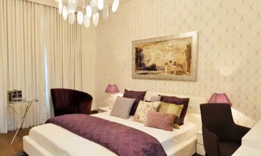 A stunning bedroom with a white and purple color scheme and a chandelier.