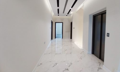 Bright corridor with marble flooring, recessed lighting, and two elevators on the right side.