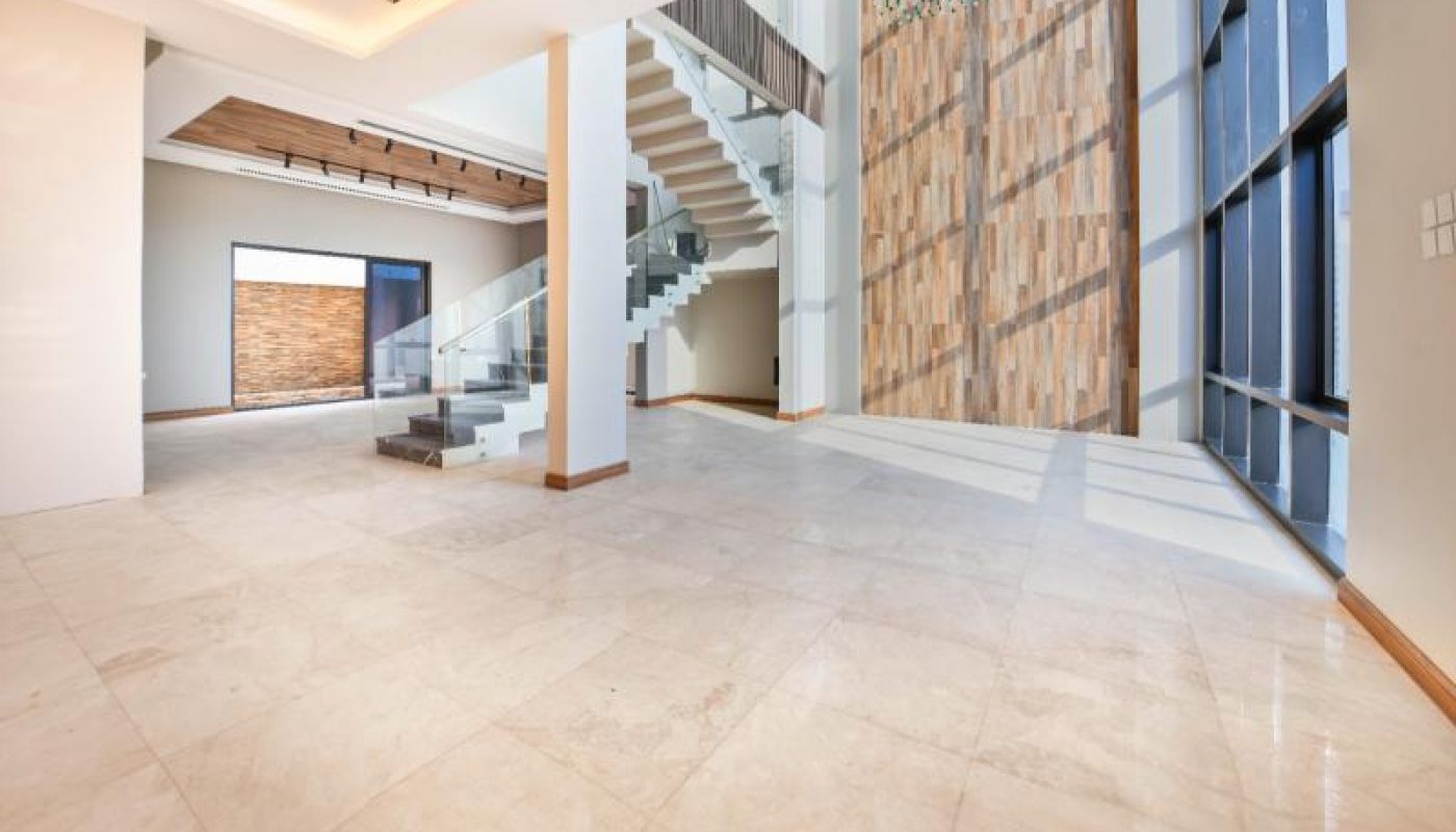 Spacious modern foyer with marble flooring, tall windows, a central staircase with glass railings, and a decorative wood accent wall.