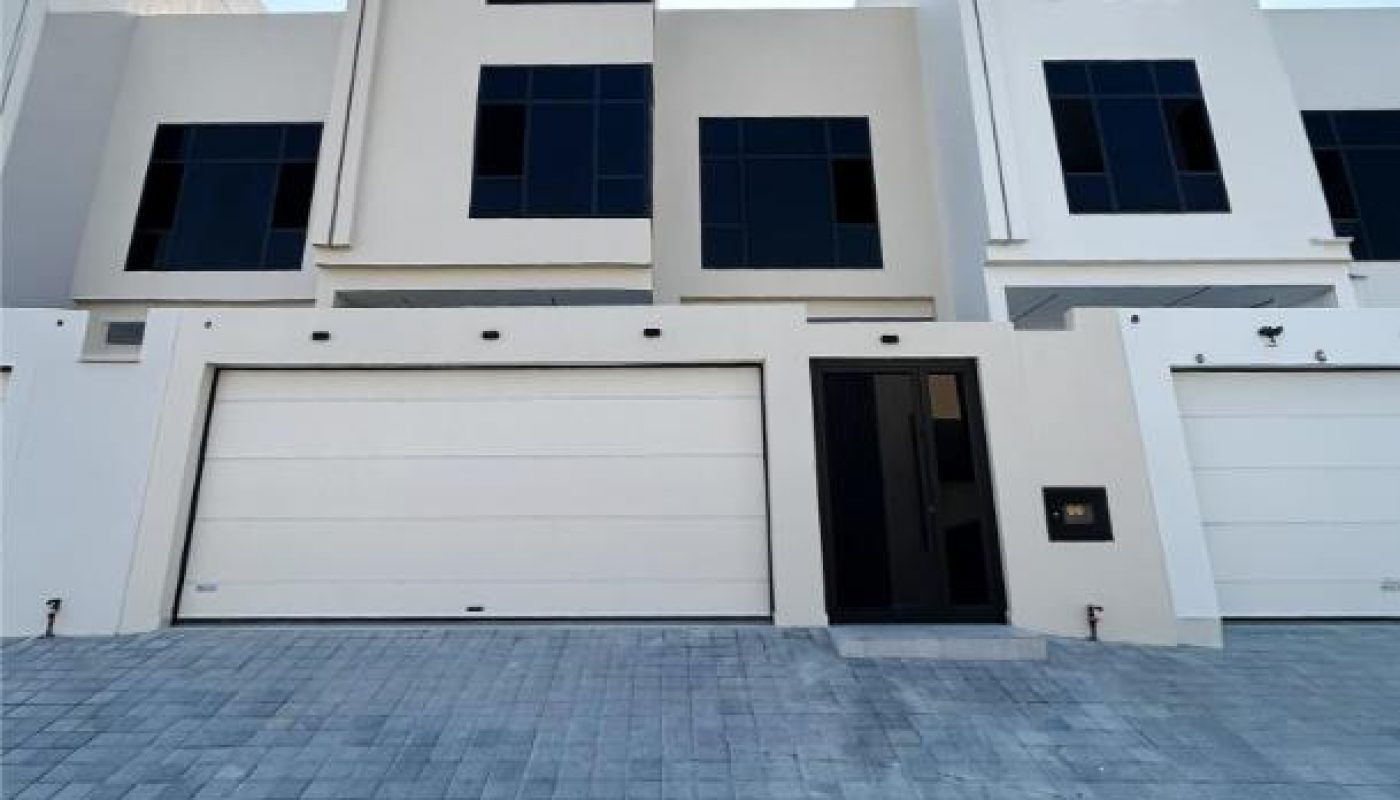 Modern white townhouse with large black-trim windows, double garage doors, and a paved driveway under a clear blue sky.