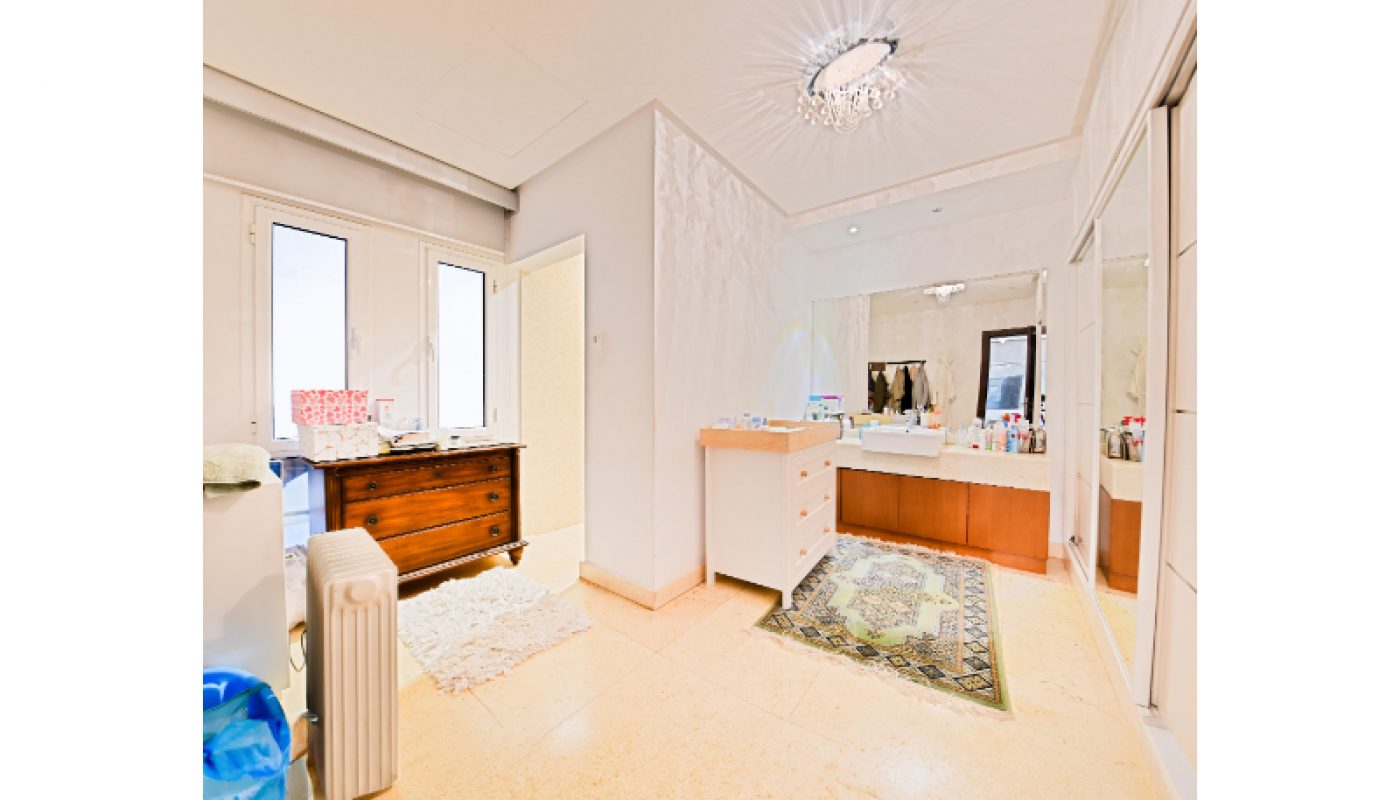 Spacious bathroom with a vanity, sink, mirror, wooden chest of drawers, rug, and large windows letting in natural light.
