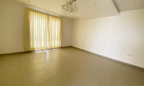 An empty room with a chandelier and white walls in an Amazing 6BR Villa for Sale in Al Markh.