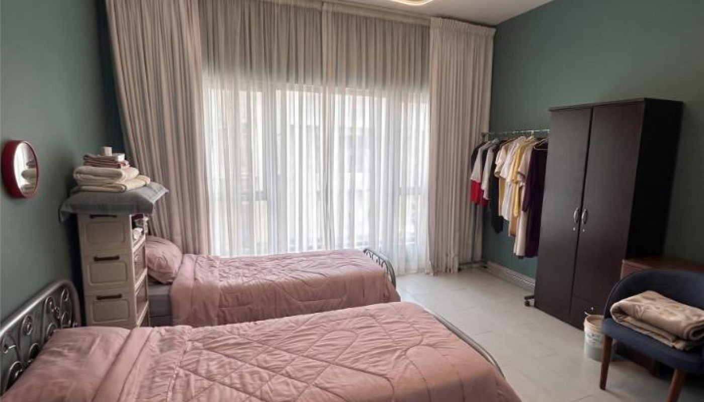 A bedroom with two beds, a wardrobe, and a clothing rack with clothes.