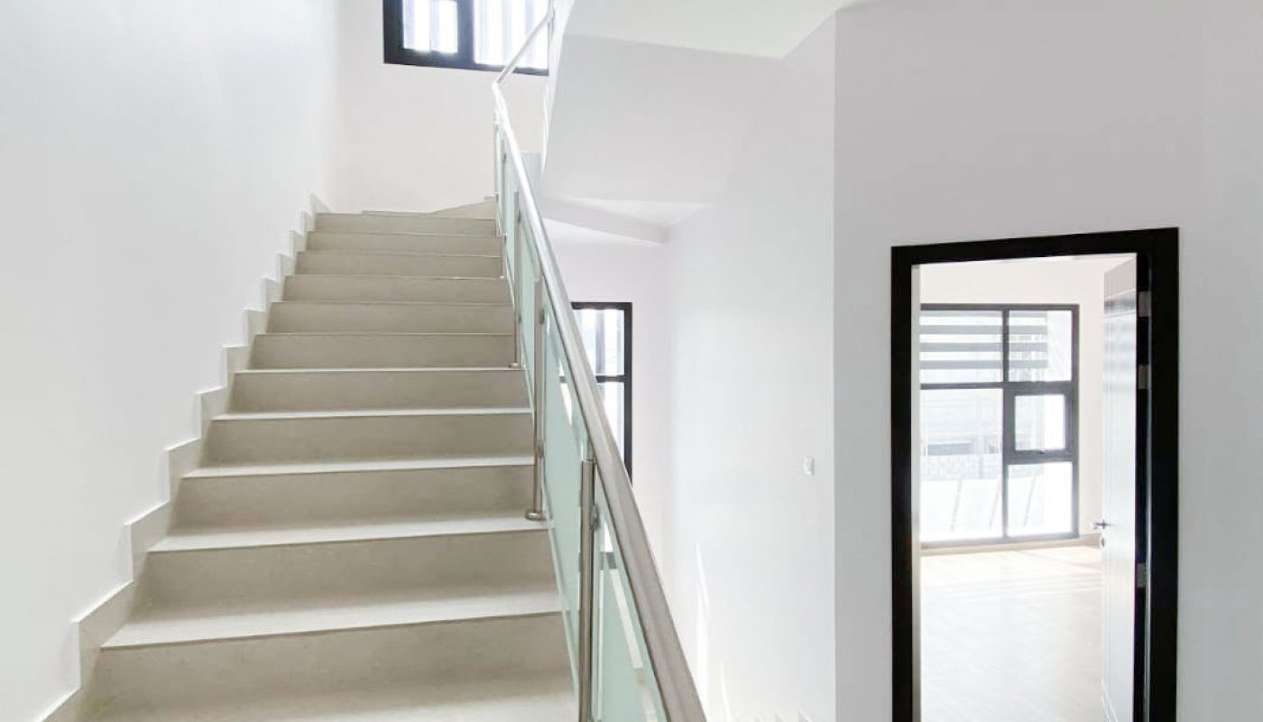 Modern indoor staircase with glass railing leading to an upper floor, adjacent to a doorway and large windows letting in natural light.