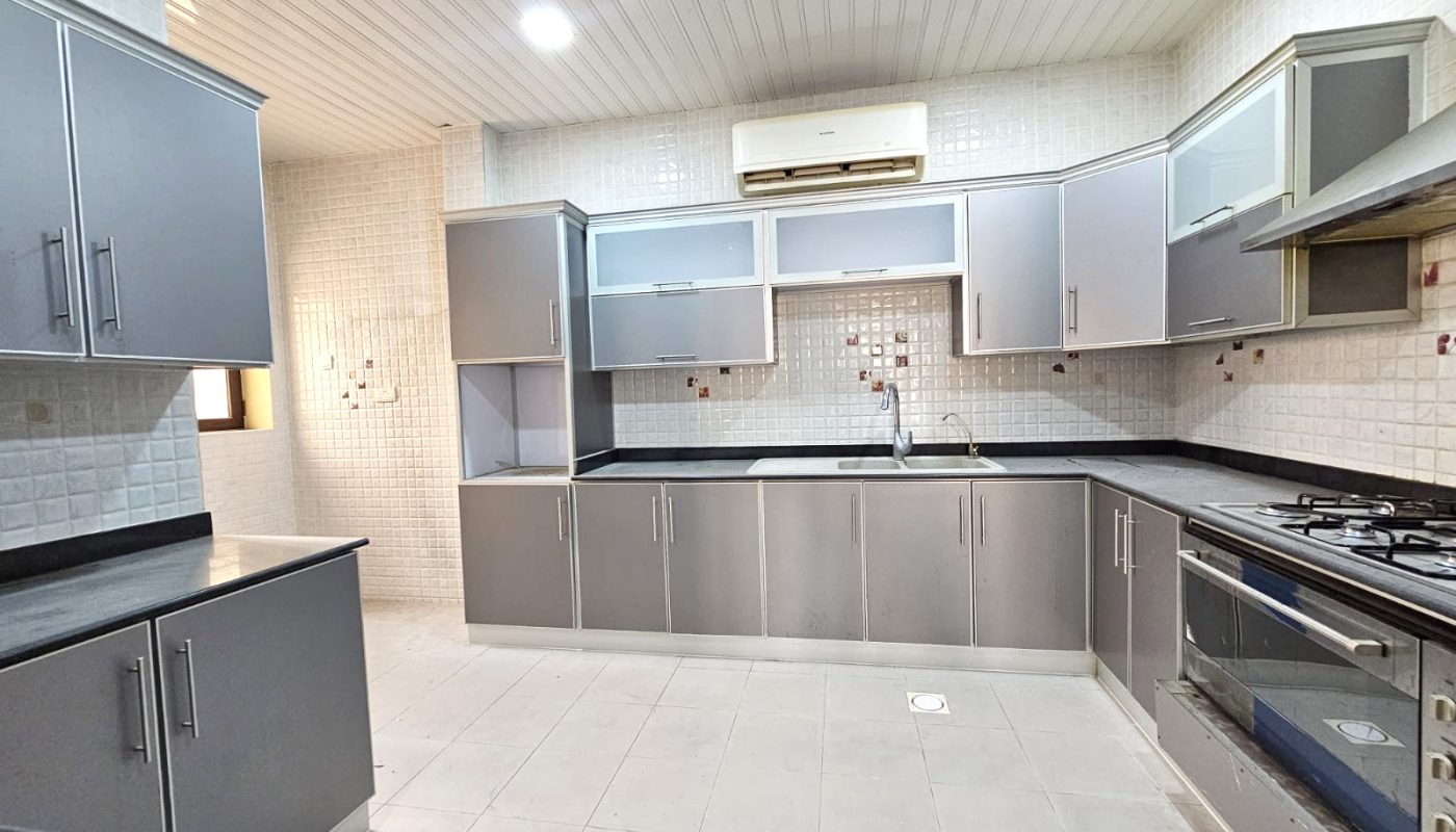 Modern kitchen with gray cabinets, white tiled walls and floor, built-in oven, gas stove, sink, and an air conditioning unit above the sink area.