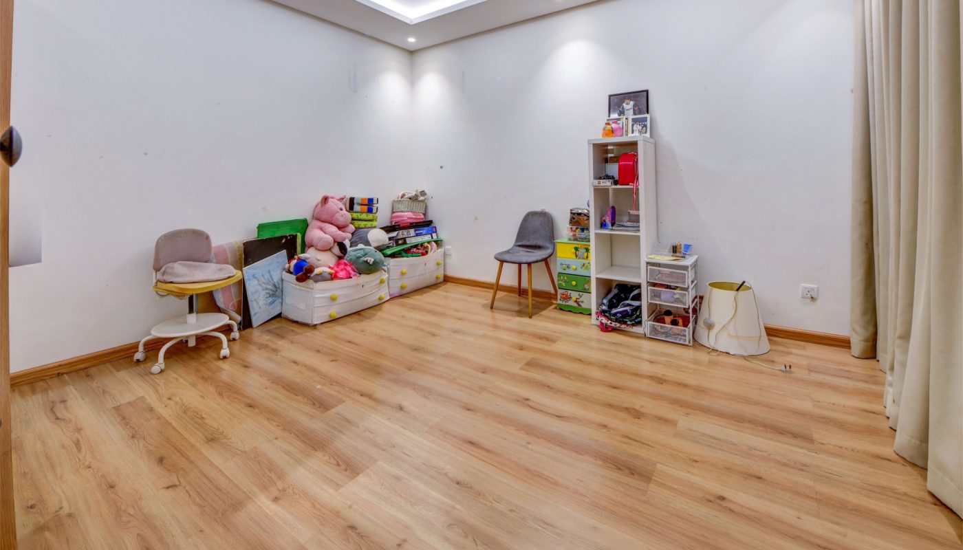 Spacious room with wooden floor, two gray chairs, toys, and shelves neatly arranged against white walls under recessed ceiling lights.