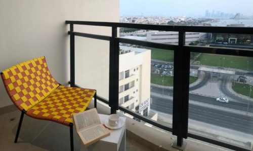 A luxury apartment balcony in the Busaiteen area with a stunning view of the city, featuring a vibrant yellow chair.