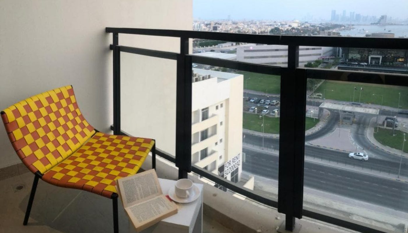 A luxury apartment balcony in the Busaiteen area with a stunning view of the city, featuring a vibrant yellow chair.