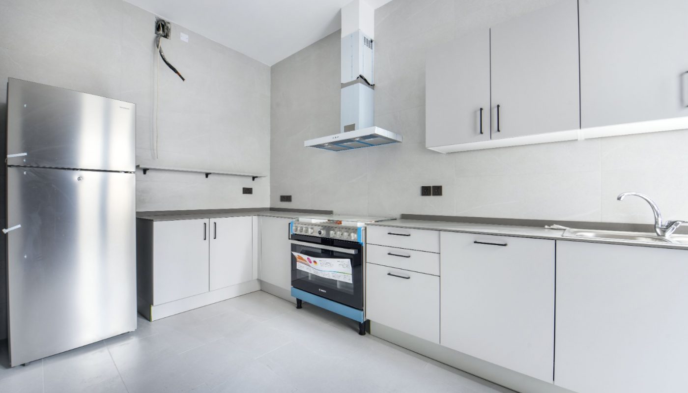 Modern kitchen with a stainless steel fridge, oven with range hood, white cabinets, and a single-basin sink on a grey countertop.