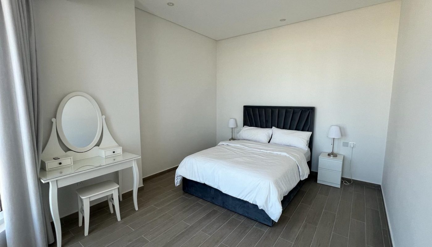 A cozy flat in Amwaj available for rent, featuring a bedroom with a comfortable bed, dresser, and mirror.