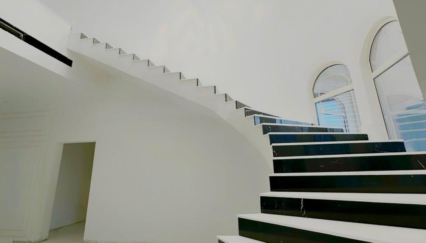 A modern interior with a black and white staircase curving upward, white walls, and large arched windows letting in natural light.