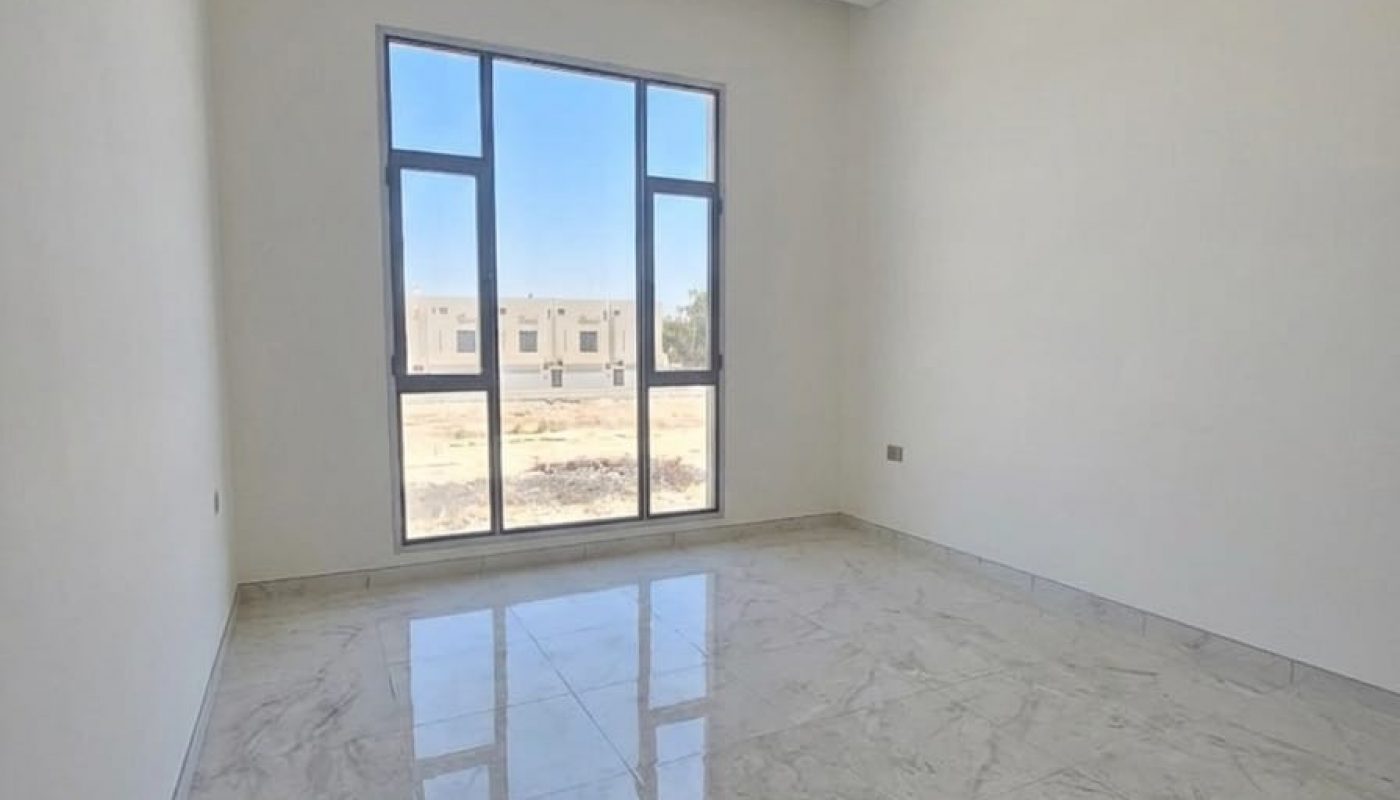 Empty room with white walls, large window, and marble floor tiles; natural light coming in through the window, with buildings visible outside.