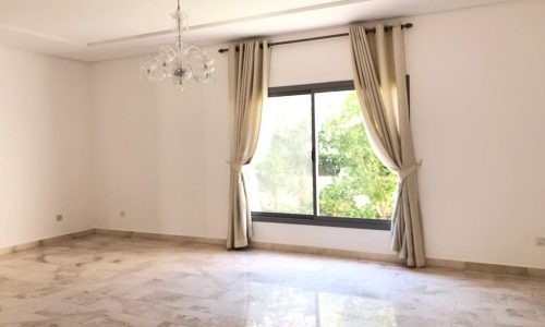 Empty living room with polished marble floor, large window with beige curtains, and a hanging chandelier.