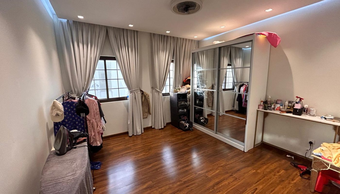A tidy room with wooden flooring, large windows with light curtains, a mirrored wardrobe, clothes racks, a table with various items, and an ironing board.