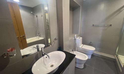 A modern bathroom in a Real Estate property featuring two sinks, mirrors, a shower, and a toilet, with tiled walls and flooring.