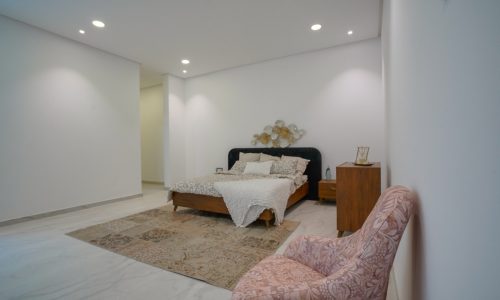 Spacious bedroom with a bed and a pink chair.