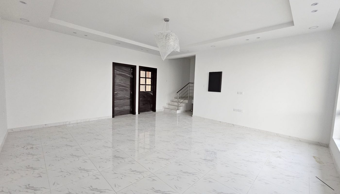 Spacious empty room with white tiled floor, white walls, and a recessed ceiling with a light fixture. A staircase is visible in the background.