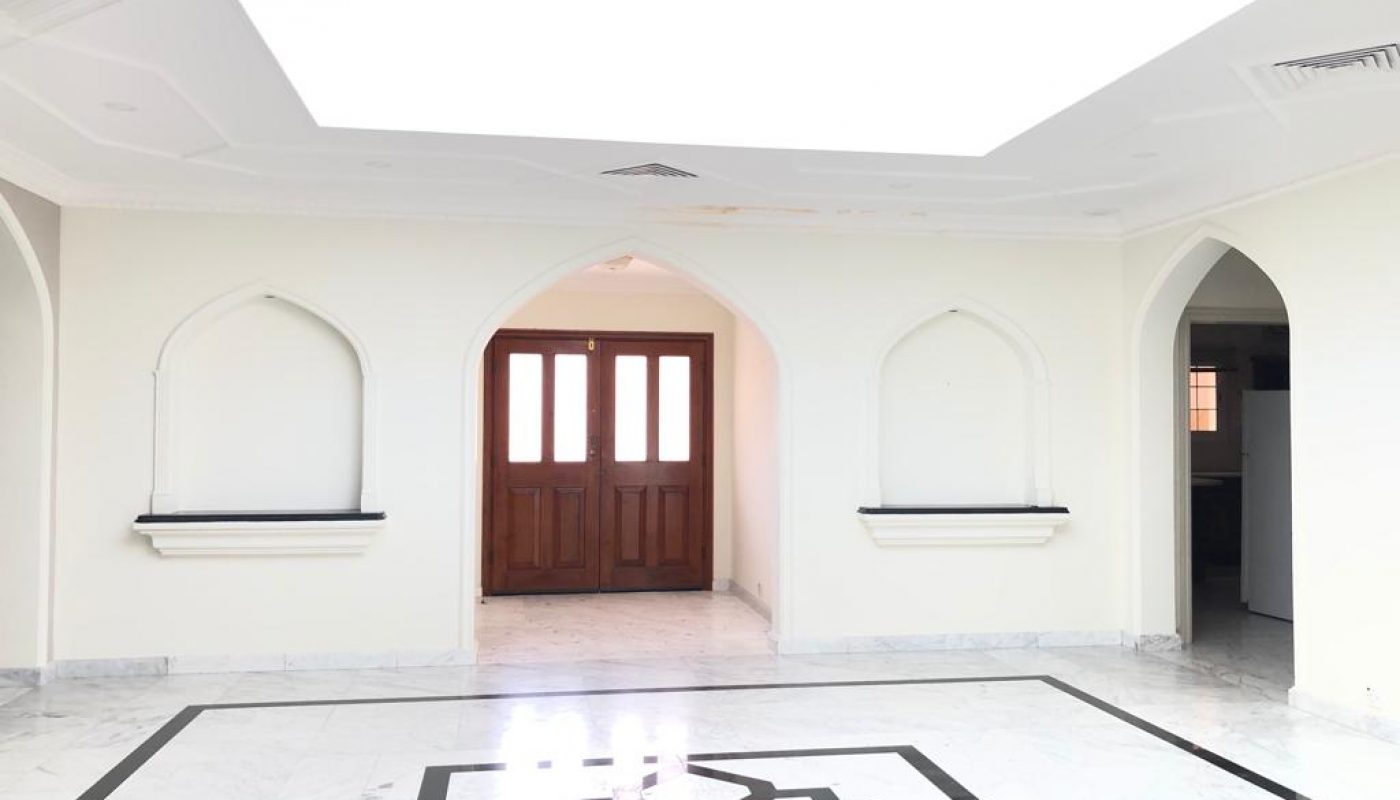 A semi-furnished, spacious room with marble flooring, an ornate black and white geometric pattern, arched wall niches, and double wooden doors under a brightly lit ceiling is one of the highlights of this stunning 3-bedroom villa.