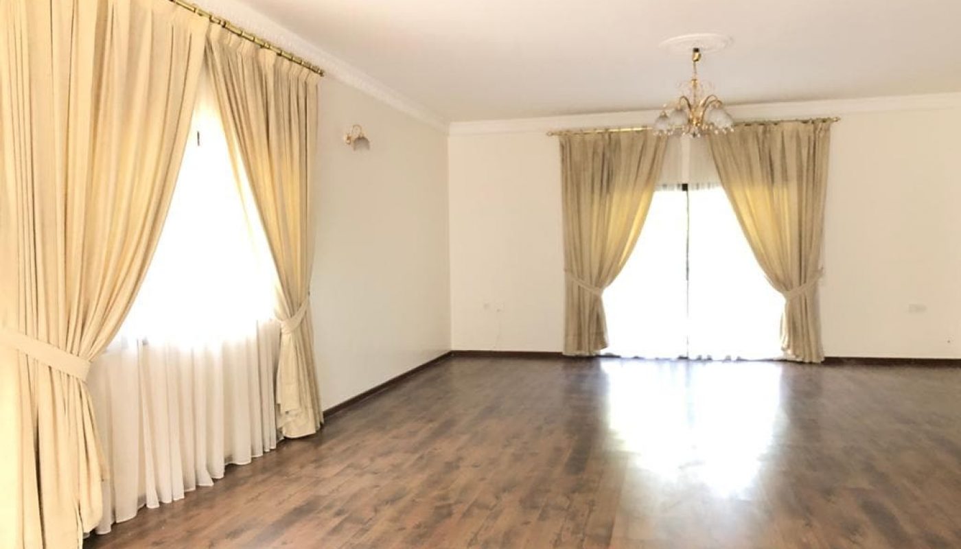 Spacious villa with polished wooden flooring and large windows draped with cream-colored curtains.