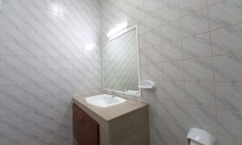 A modern bathroom with a white sink on a beige countertop, a rectangular mirror above, and white tiled walls.