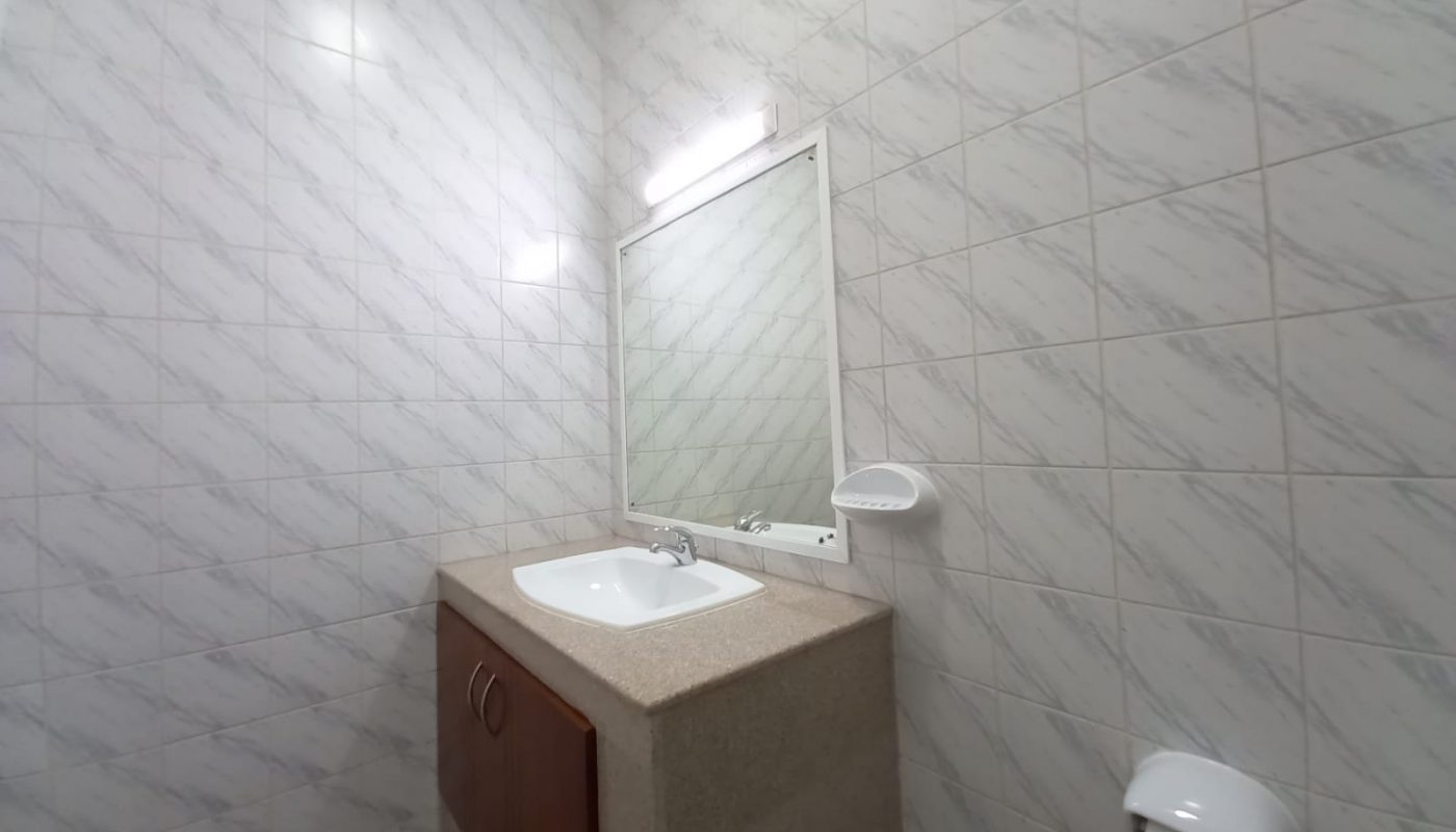 A modern bathroom with a white sink on a beige countertop, a rectangular mirror above, and white tiled walls.