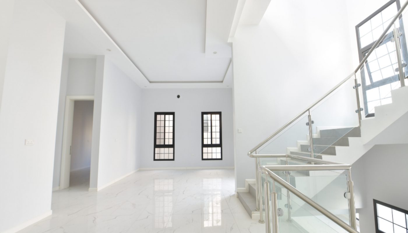 Spacious, empty room with white marble floor, white walls, two black-framed windows, and a staircase with a glass and metal railing.