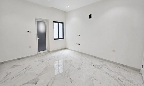 This spacious, empty room with white walls and a glossy marble floor is part of a luxurious villa. The room features a window, a door, and overhead recessed lighting, all designed to accentuate the elegance of this unique villa for sale.