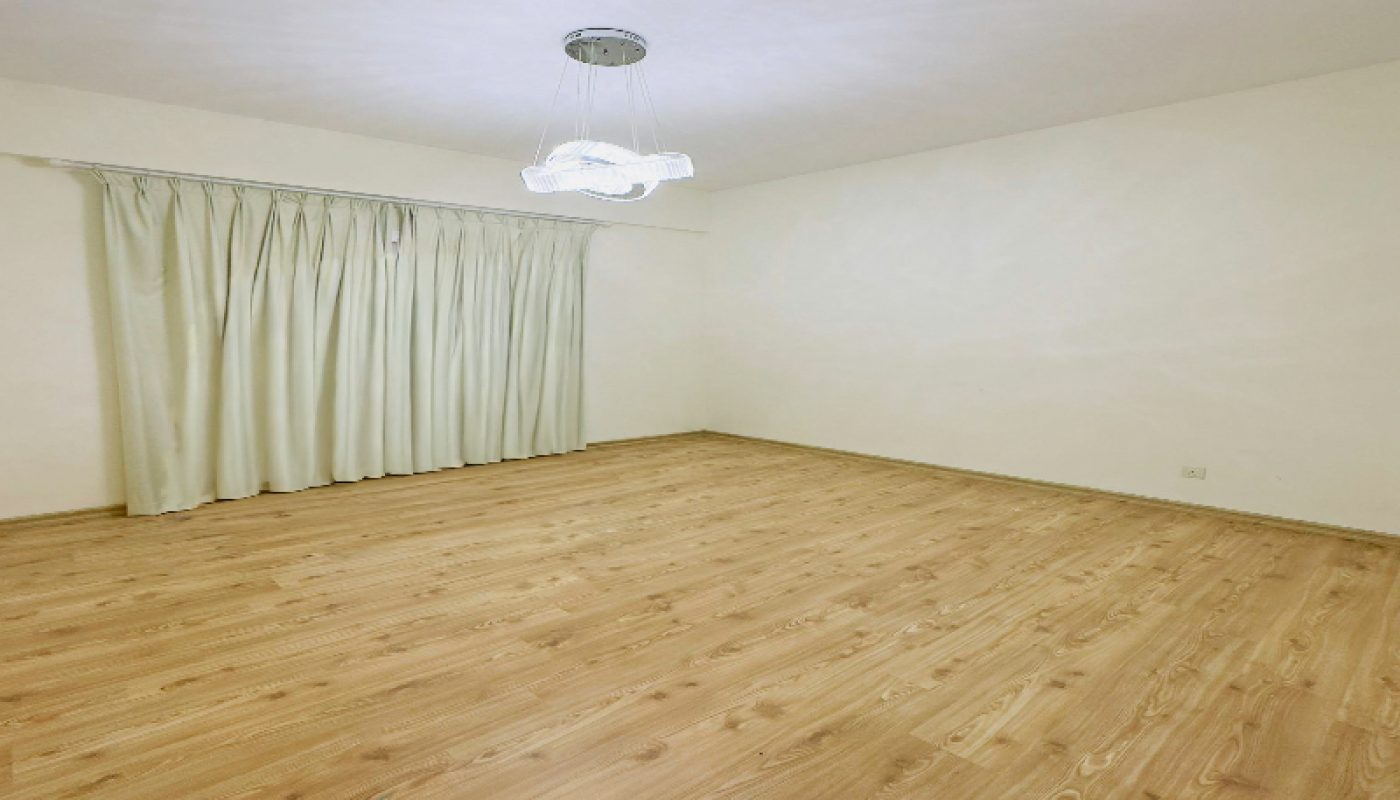 Empty room with light wood flooring, cream-colored walls, ceiling light fixture, and closed beige curtains covering a window.