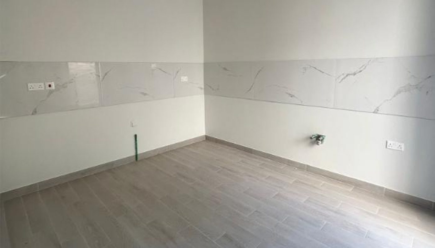 Empty room with light gray tiled floor, white and gray marble-patterned wall tiles, plumbing fixtures, and electrical outlets, possibly intended for a kitchen installation.