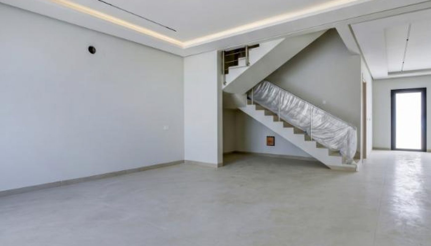 Interior view of an empty room with light tile flooring, a modern staircase with plastic sheeting, and recessed ceiling lighting.