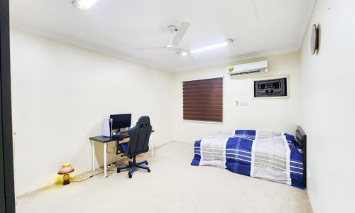 A luxury bedroom with a bed, desk, and fan in a 3 bedrooms villa for sale in Hamad Town.