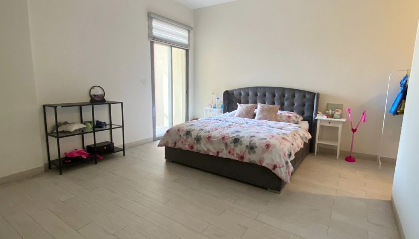 A minimalist bedroom with a double bed, side tables, shelving unit, coat rack, and large window; the floor is light-colored tile.