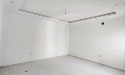 An empty room in a luxury villa with white walls and wooden floors.