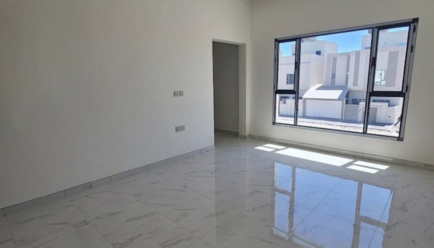 Empty room with white walls, glossy marble floor tiles, recessed ceiling lights, and a large window facing neighboring buildings in daylight.