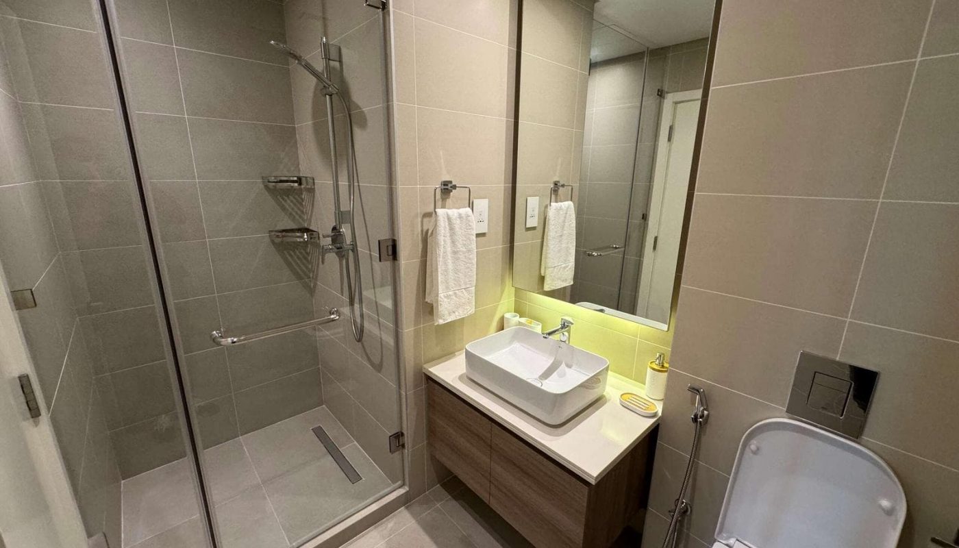 Modern bathroom interior in a luxurious apartment, featuring a glass shower cubicle, single sink vanity with a mirror, and a toilet, illuminated by soft yellow lighting.