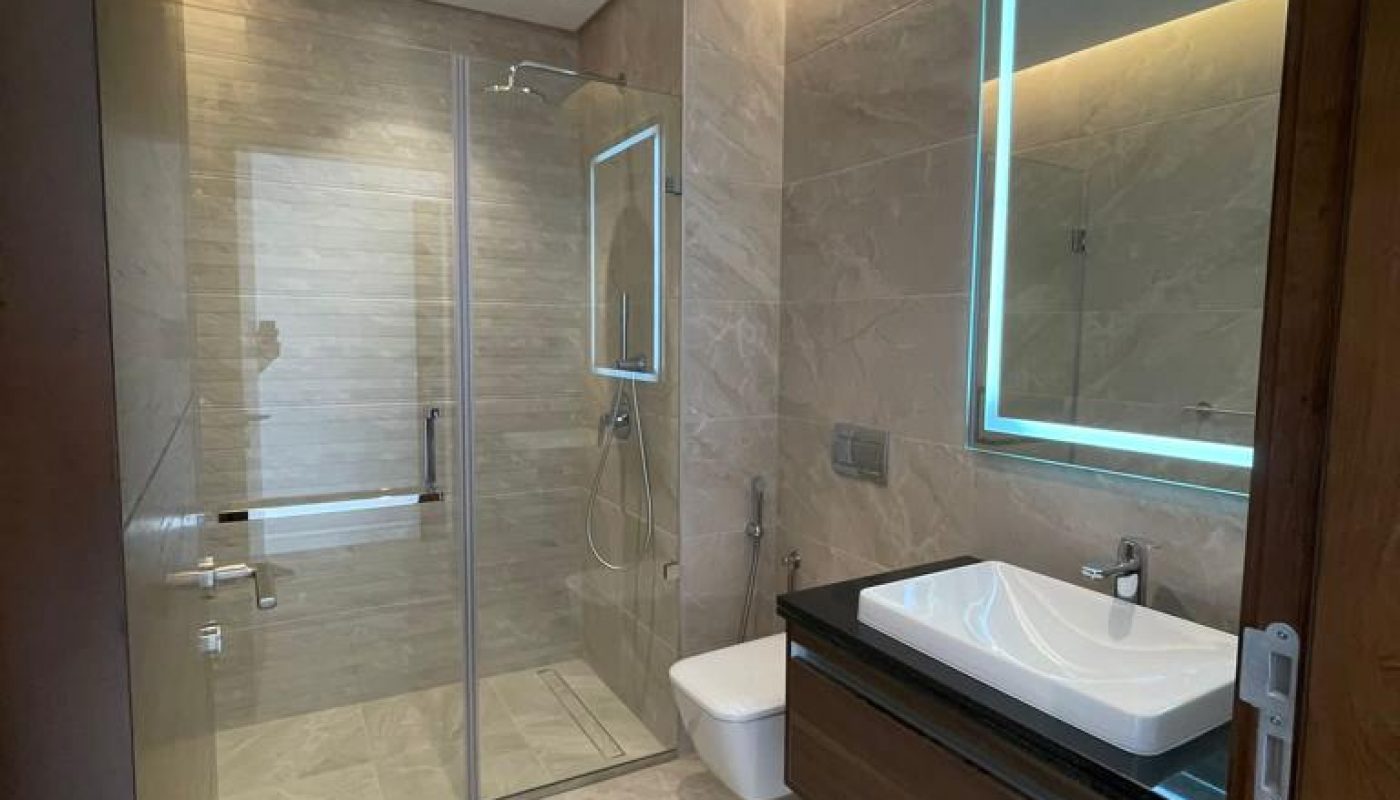 A modern bathroom with a glass shower and sink is available for sale in the Dilmunia Apartment.