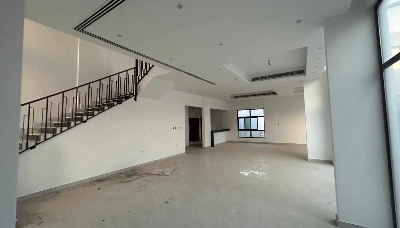 Spacious, empty modern room with large windows, a staircase with a metal railing, and an open-concept design. Floor appears unfinished.
