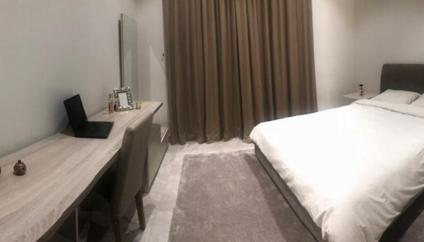 A luxury apartment in Busaiteen for sale, featuring a spacious bedroom with a comfortable bed and a functional desk.