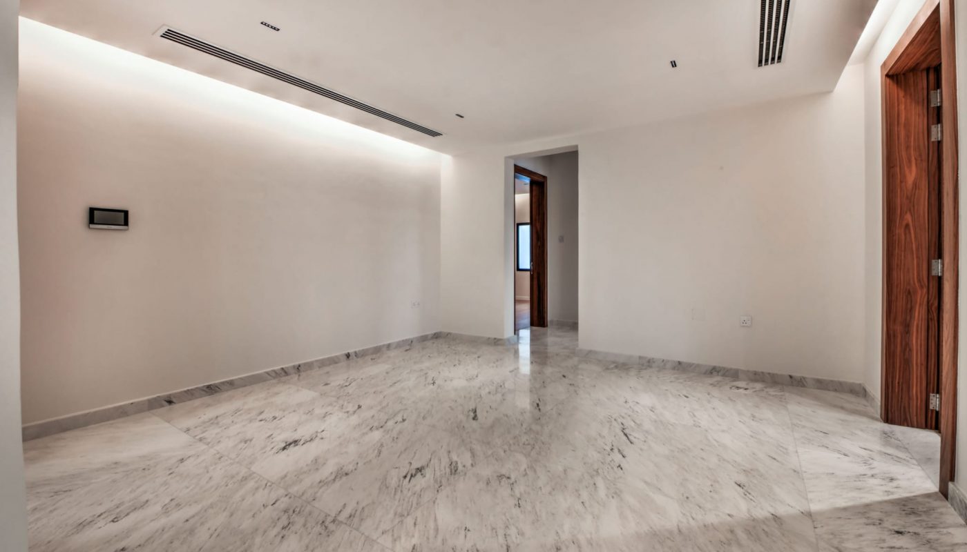 Empty room with white walls, recessed lighting, marble flooring, and wooden door frames. Multiple openings lead to other parts of the building. No furniture or decor is present.