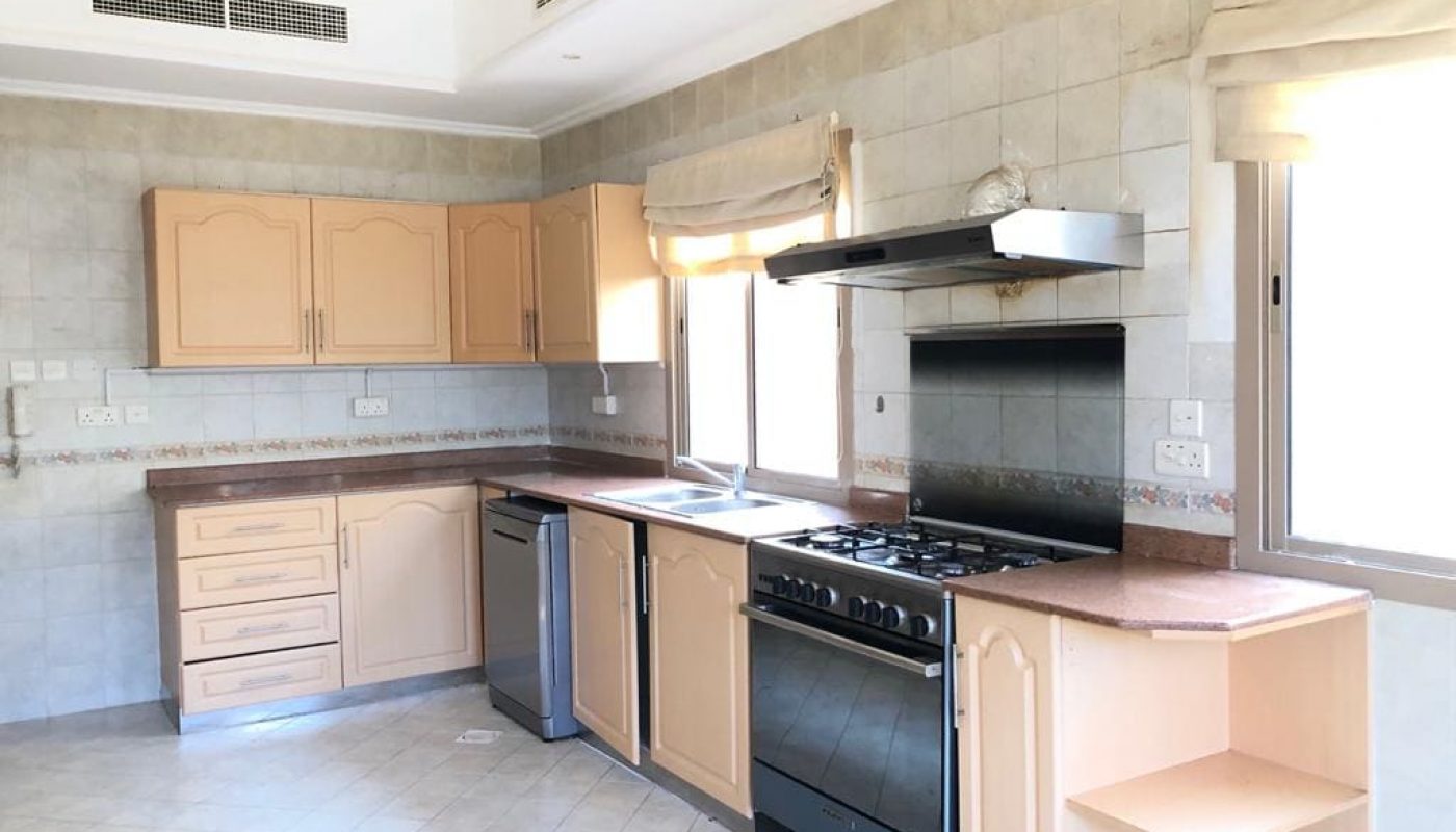 A modern kitchen with light wood cabinets, a stainless steel stove, dishwasher, sink, and granite countertops. The room features tiled walls and floor, with windows providing natural light.