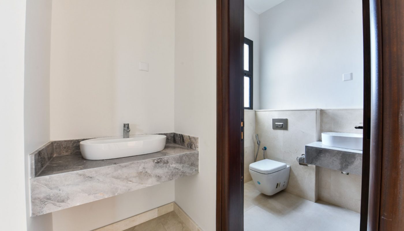 Modern bathroom with two separate areas, one featuring a sink on a marble countertop, and the other with a wall-mounted toilet and a second sink under a window.