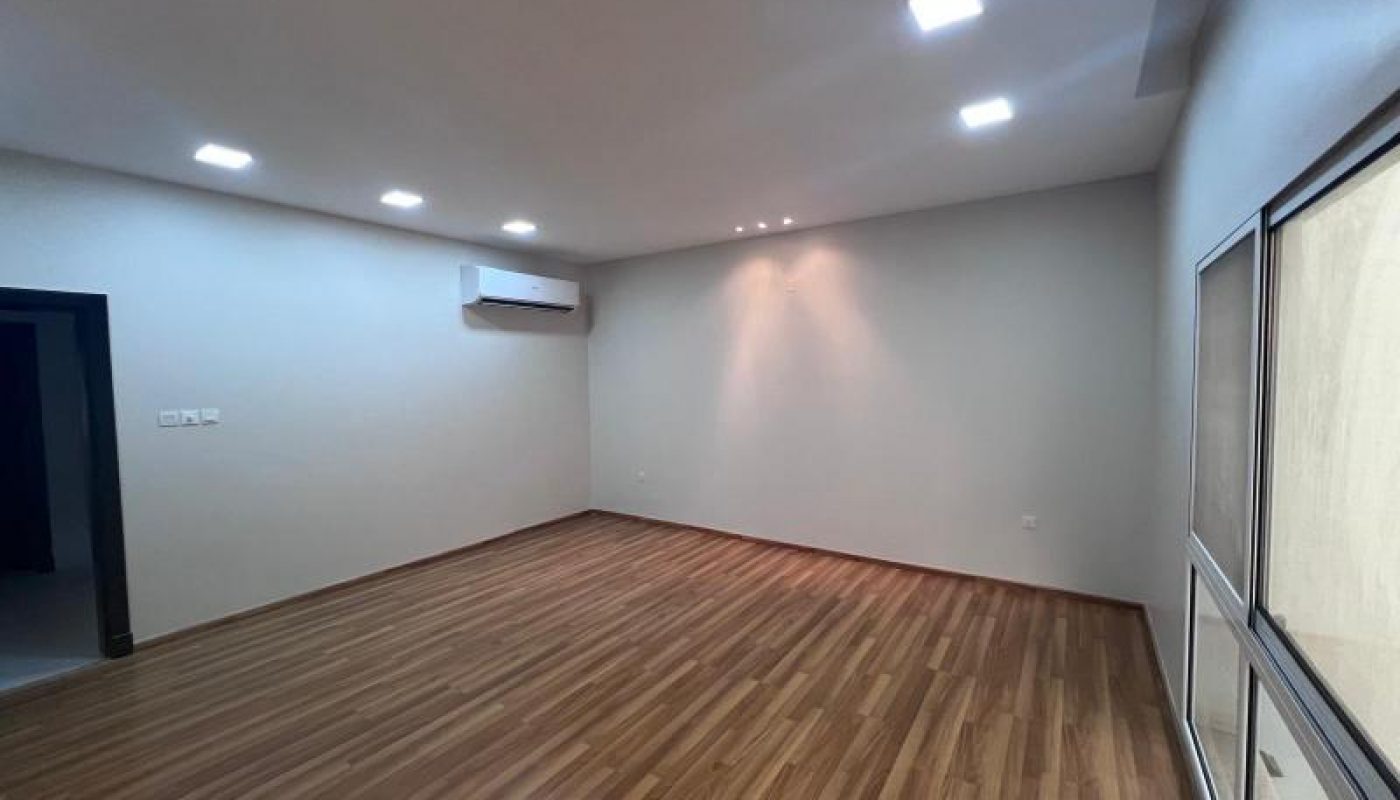 Empty room with wood flooring, recessed ceiling lights, an air conditioning unit on the wall, and large windows on the right side.