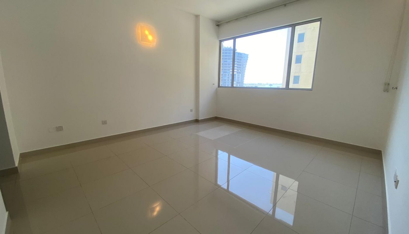 Empty room with tiled floor, white walls, a large window letting in natural light, and a view of buildings outside.
