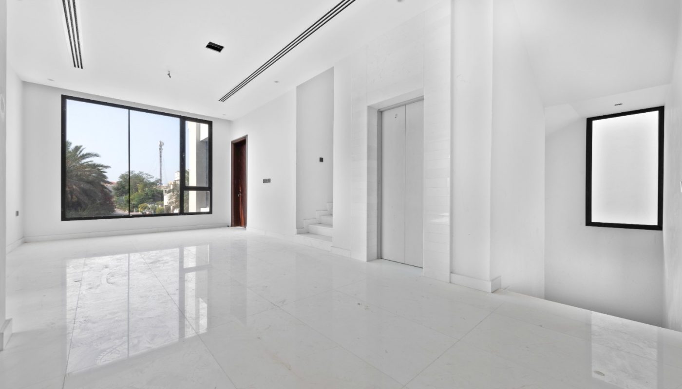 Spacious, empty white room with large windows, marble floor, elevator door, a small staircase, and a view of palm trees outside.
